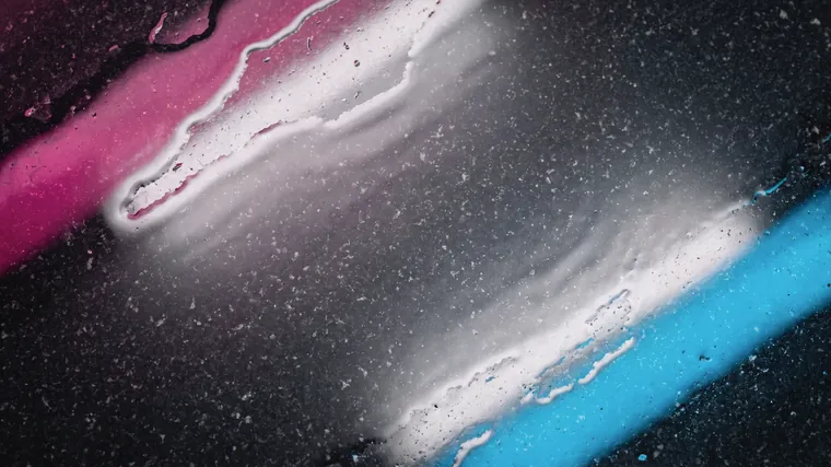 Wet black stone at close range, with bands of magenta, white and cyan running diagonally across it.