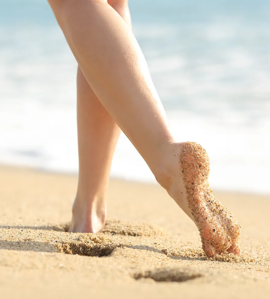 Bare legs mid-stride on wet sand, footprints trailing behind, surf blurred in the distance.