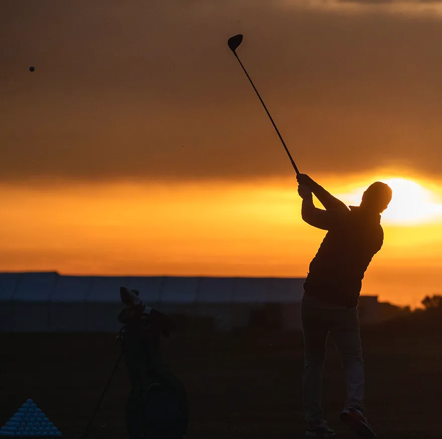 A golfer at full follow-through silhouetted against a burnt-orange sunset.