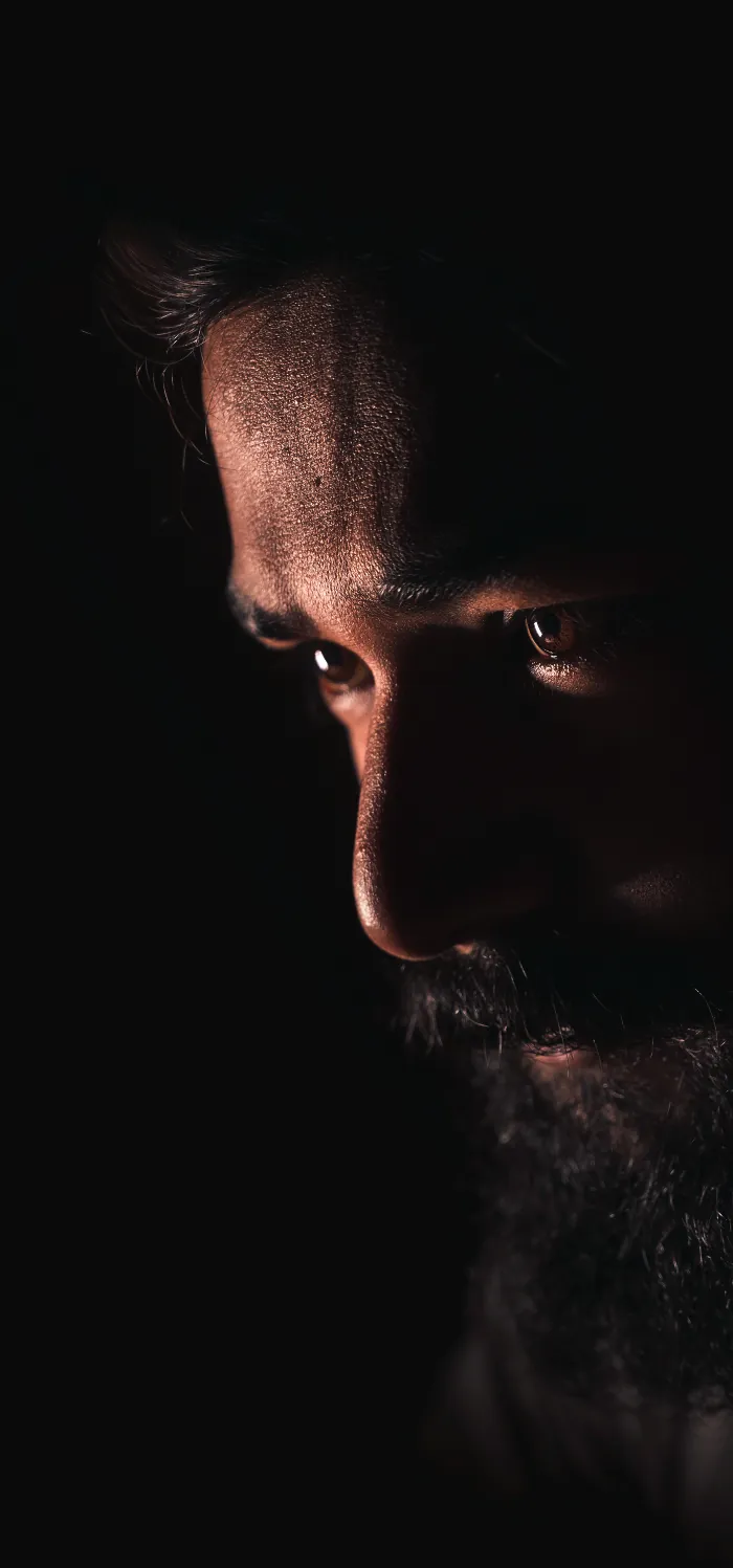 A bearded man lit by a single hard light from the left against a black ground, from the men's price card cover.