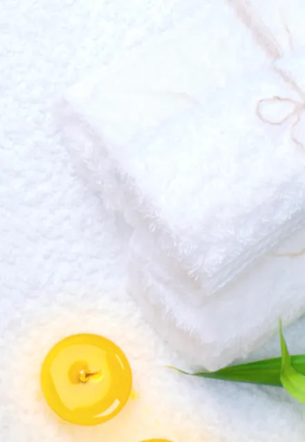 Folded white towels with yellow gel candles and a bamboo leaf beside them.